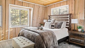 A bedroom with a wooden ceiling, a large bed with a headboard, two bedside tables, and a window with blinds. - Guest FAV Luxury Sun Chalet + Hot Tub + BBQ (Big Bear Lake)
