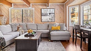 A cozy living room with a wooden ceiling, a gray sectional sofa, a coffee table, and a dining area with a table and chairs. - Guest FAV Luxury Sun Chalet + Hot Tub + BBQ (Big Bear Lake)