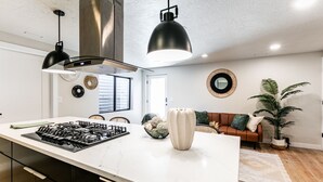 Una cocina moderna con una isla grande, lámparas colgantes negras y una campana extractora de acero inoxidable.