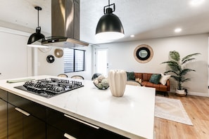 Una cocina moderna con una isla grande, lámparas colgantes negras y una campana extractora de acero inoxidable.