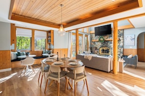 A wooden interior with a dining area, stone fireplace, and large windows.