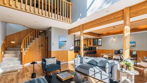 A spacious living area with a staircase, wooden beams, and a dining area. - Palisades Cabin Retreat | Hot Tub•A/C•EV•Views (Alpine Meadows)