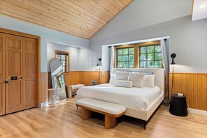 A bedroom with a large bed, wooden ceiling, and a window with curtains.