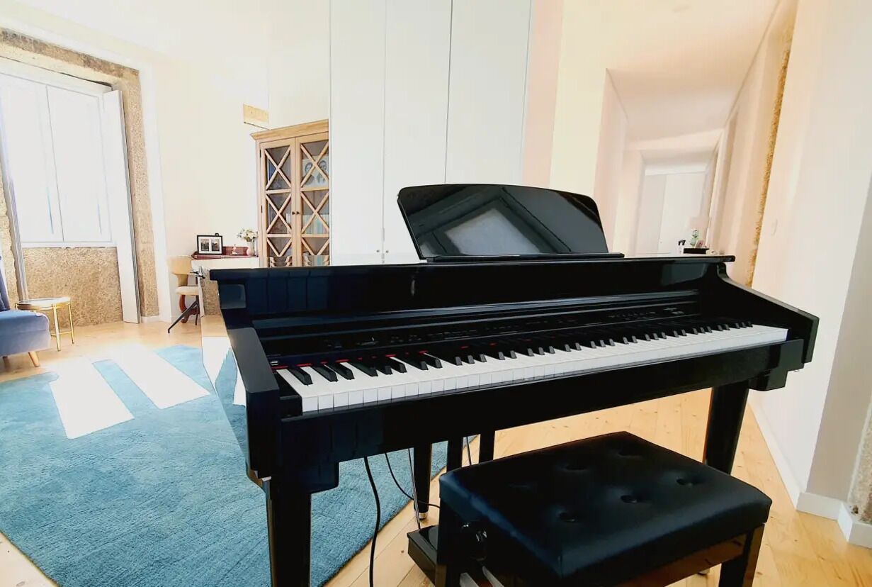 Un piano noir dans une pièce où se trouvent un tapis bleu, un meuble en bois et une porte.