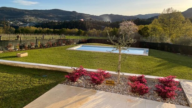 Ein angelegter Garten mit Schwimmbad, einem kleinen Baum und Blick auf ferne Hügel.