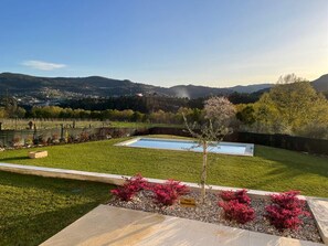 Ein angelegter Garten mit Schwimmbad, einem kleinen Baum und Blick auf ferne Hügel.
