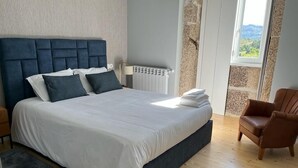 Ein Schlafzimmer mit einem großen Bett, einem Heizkörper, einem Fenster mit Blick und einem Sessel.