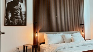 Une chambre à coucher comprenant un lit, des tables de chevet, un luminaire fixé au mur et un tableau encadré accroché au mur.