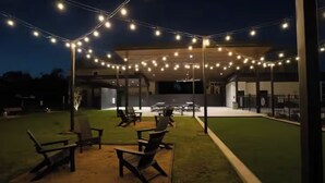 Un espace extérieur aménagé avec des guirlandes lumineuses, des chaises et un bâtiment en arrière-plan.