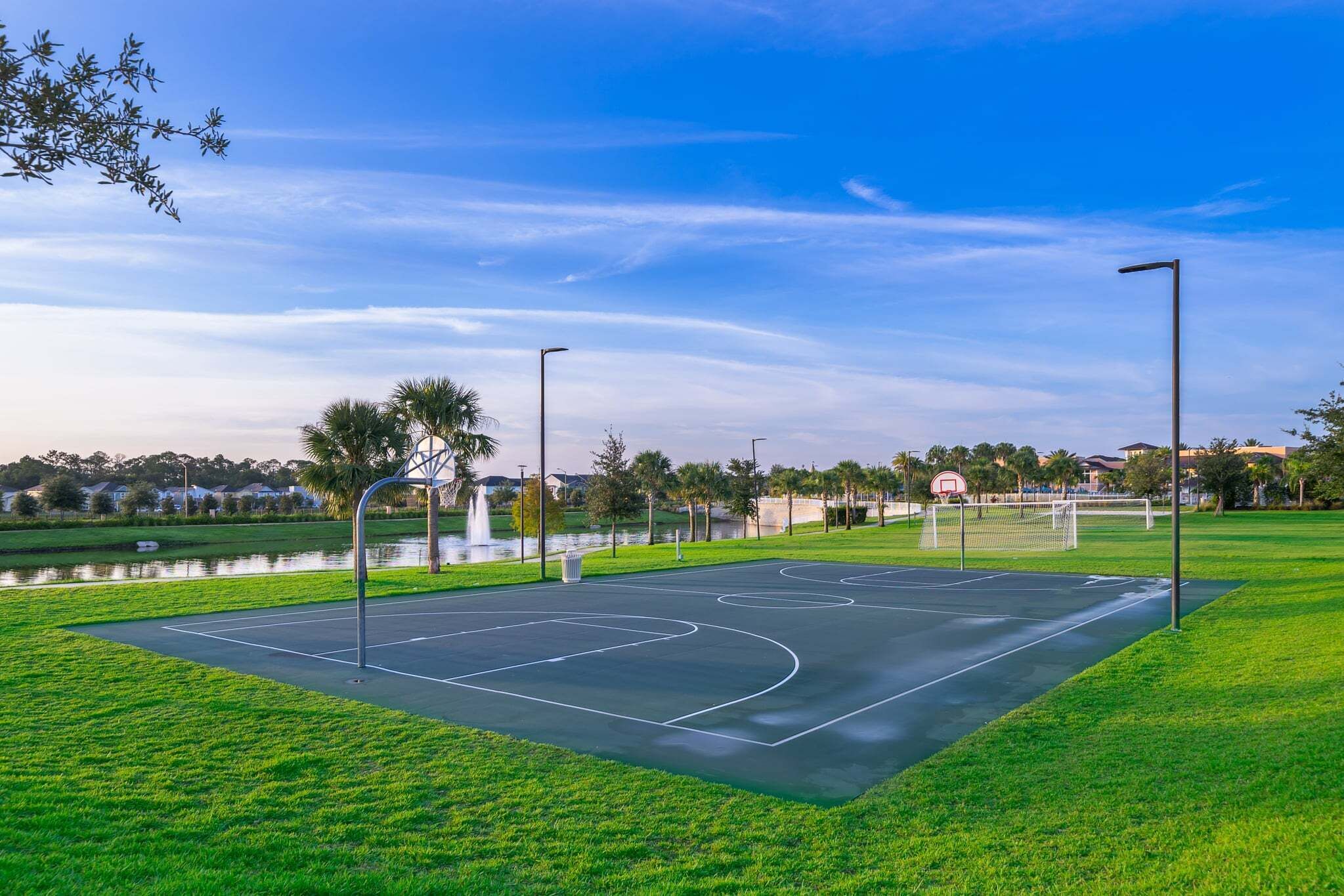 An outdoor basketball court with a water feature in the background.