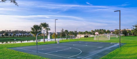An outdoor basketball court with a water feature in the background.