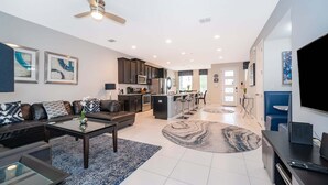 A modern living room with a sofa, coffee table, and TV. There is a kitchen area with cabinets and a microwave. - 3BR Solara Resort Home with Private Pool, BBQ & Resort Amenities Near Disney (Kissimmee)