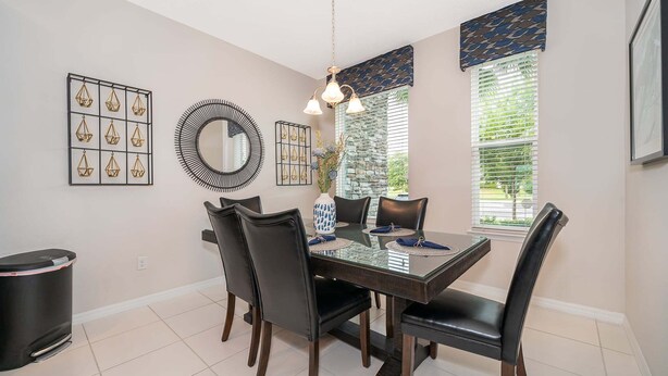 A dining area with a rectangular table, six chairs, a round mirror, and decorative wall art. - 3BR Solara Resort Home with Private Pool, BBQ & Resort Amenities Near Disney (Kissimmee)