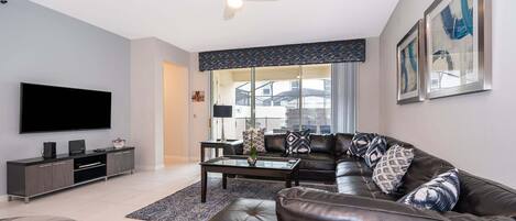 Un salon moderne doté d’un téléviseur à écran plat, d’un canapé en cuir, d’une table basse et d’un ventilateur de plafond.