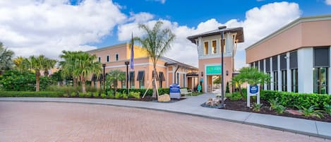A hotel entrance with a paved walkway, palm trees, and a clear blue sky.