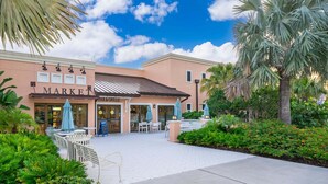 A building with a 'MARKET' sign and a 'BAR & GRILLE' sign, outdoor seating with umbrellas, and a paved walkway. - 3BR Solara Resort Home with Private Pool, BBQ & Resort Amenities Near Disney (Kissimmee)