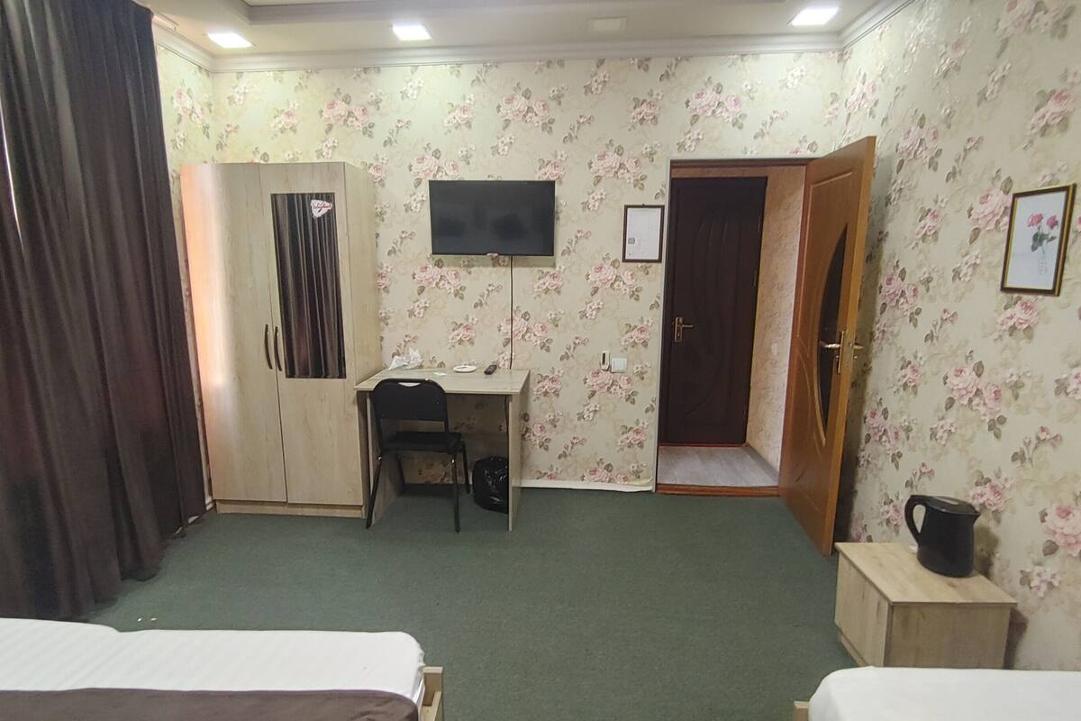 A hotel room with a bed, a desk with a chair, a wardrobe, a television, and a door.