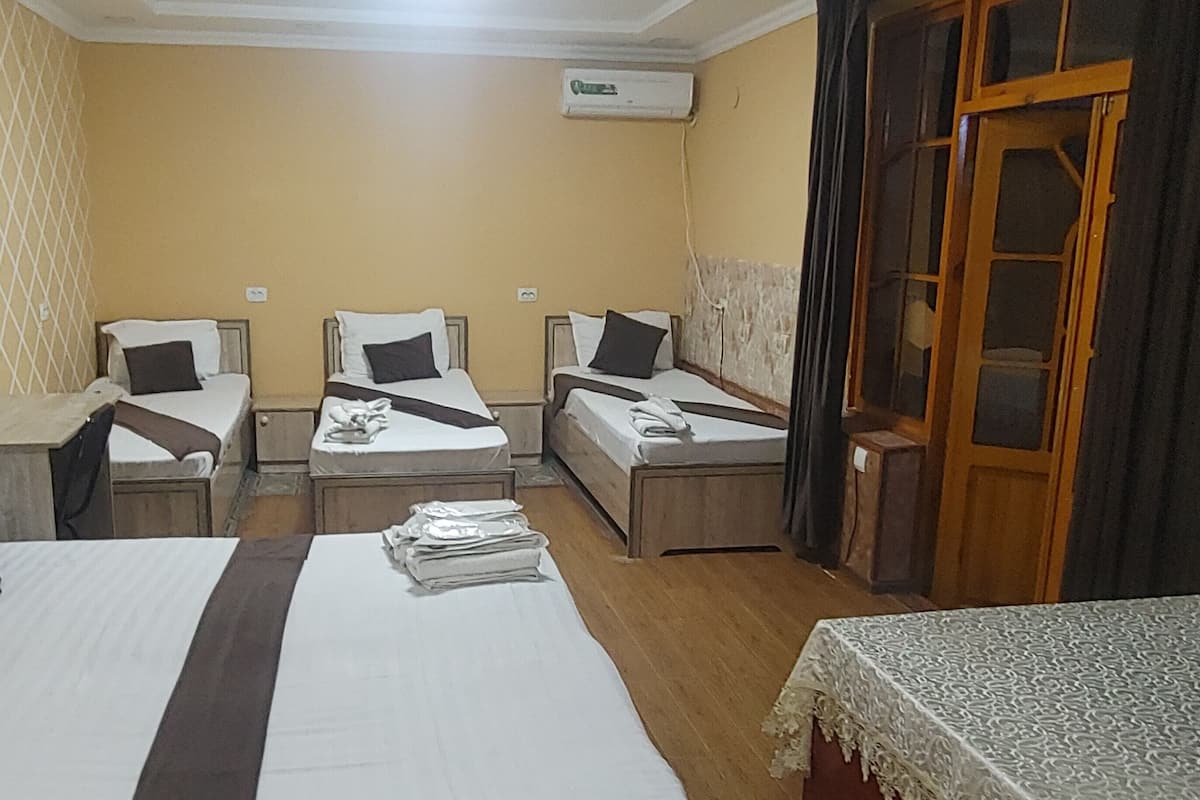 A hotel room with three single beds, a wooden wardrobe, a small table, and a patterned tablecloth.