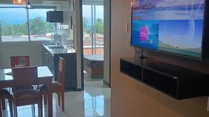 Ein modernes Wohnzimmer mit flachbildfernseher an der Wand, einem Essbereich mit Stühlen und Tisch sowie einer Küchenzeile mit Herd und Spüle.