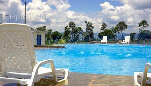 A swimming pool with water jets, surrounded by white chairs and trees. - APARTAMENTOS CERCA AL PARQUE DEL CAFE  (Montenegro)