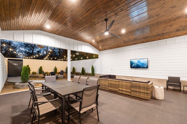 An outdoor patio with a dining table, chairs, and a seating area with a TV mounted on the wall. - North Nashville 15mins to Broadway Luxury Listing (Goodlettsville)