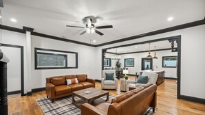 A spacious living room with leather sofas, a coffee table, and a dining area with a chandelier. - North Nashville 15mins to Broadway Luxury Listing (Goodlettsville)