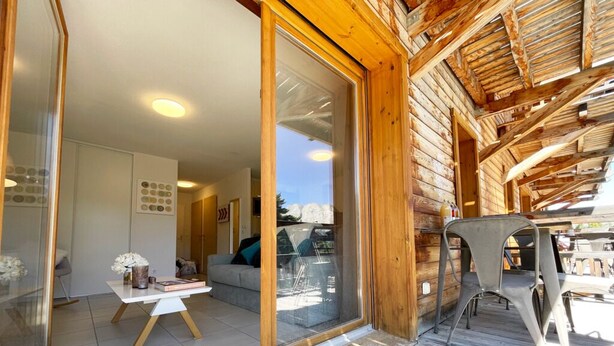 A wooden cabin with a glass door leading to a living area, a small table with a vase, and a chair outside.