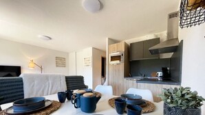 A modern kitchen with a built-in oven and a dining area with a white table set with blue dishes and a potted plant.
