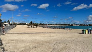A beach with a wide promenade, palm trees, and beach umbrellas. - Luxury 3 bedroom villa overlooking golf course with private pool and Wi-fi (Caleta De Fuste)