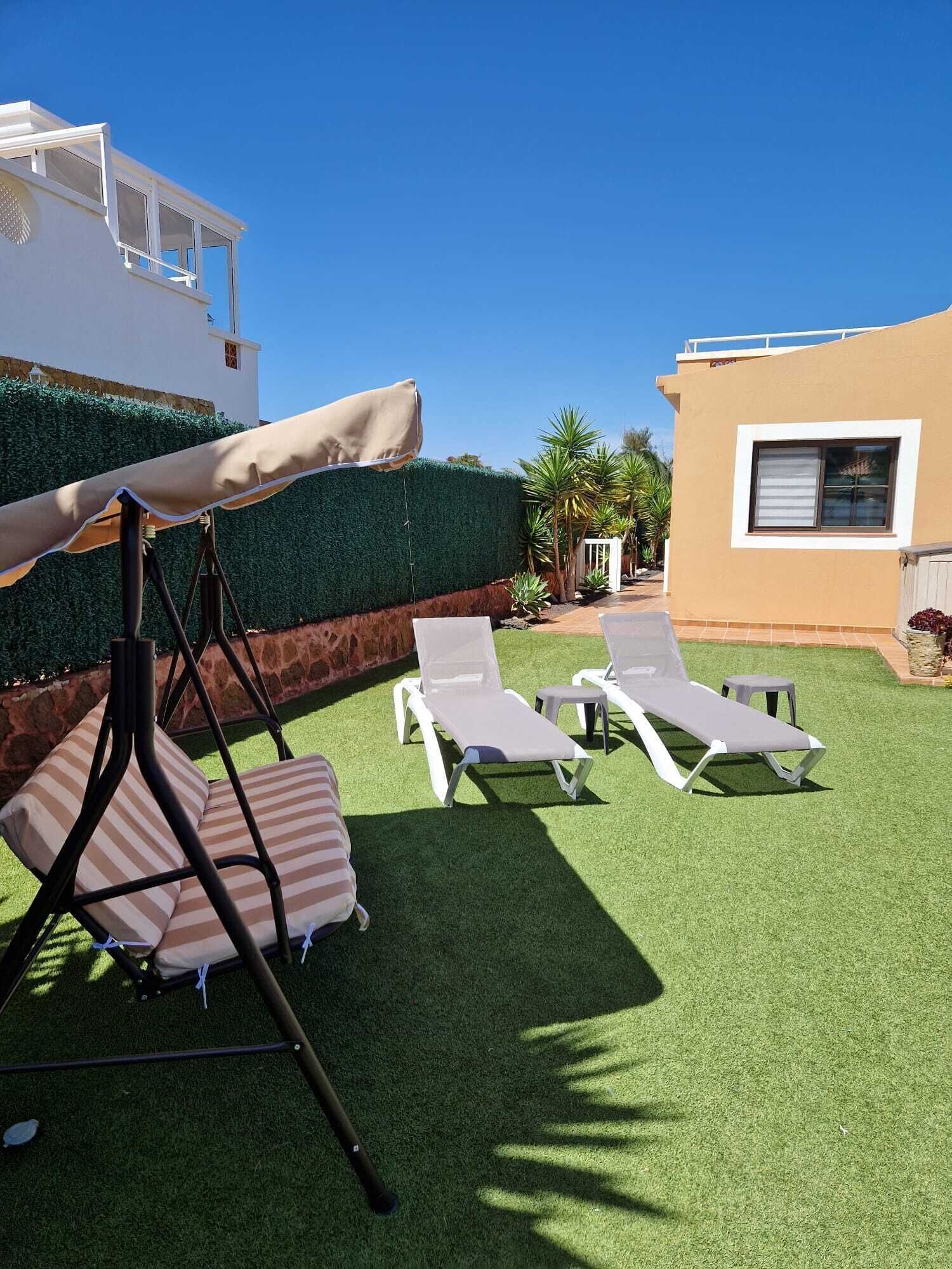 A backyard with artificial grass, a swing set, and two lounge chairs.