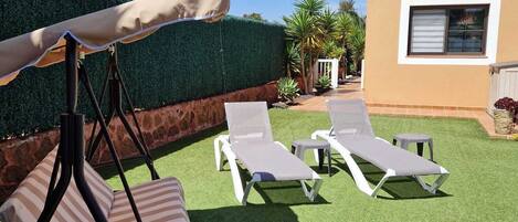 A backyard with artificial grass, a swing set, and two lounge chairs.