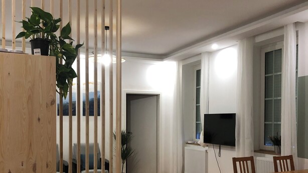 Ett modernt vardagsrum med en trätrappa, en matplats med bord och stolar, en tv och en krukväxt.