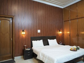 Een slaapkamer met een wand van houten panelen, een bed met wit beddengoed, twee nachtkastjes en wandlampen.