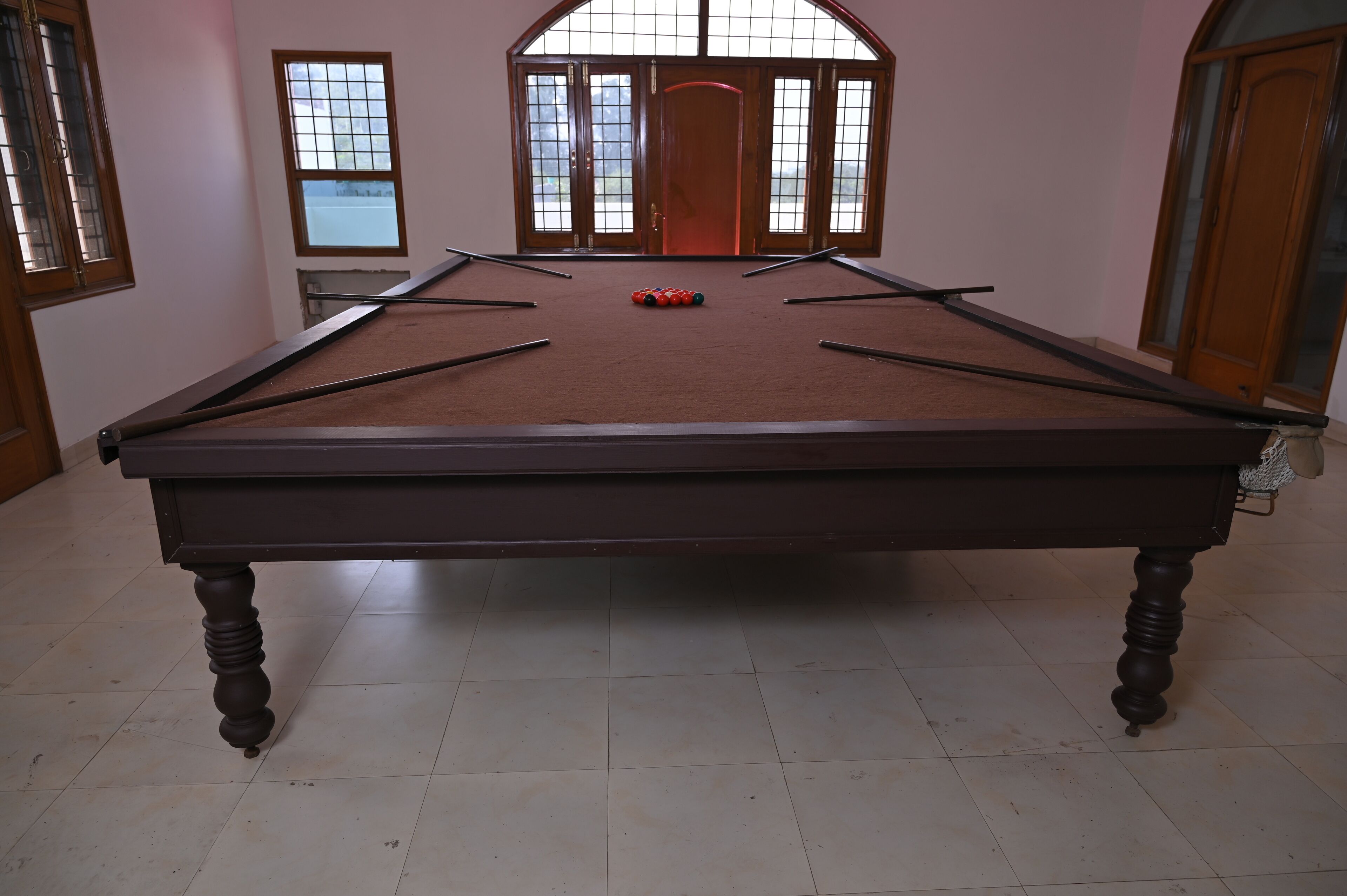 A pool table with a red felt surface, wooden legs, and a set of pool cues.