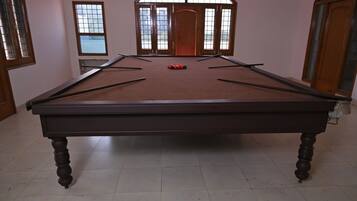 A pool table with a red felt surface, wooden legs, and a set of pool cues.