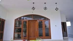 Ein moderner Eingangsbereich mit Holztür, großen Glasflächen, Pflanzkübeln und geometrischen Pendelleuchten.