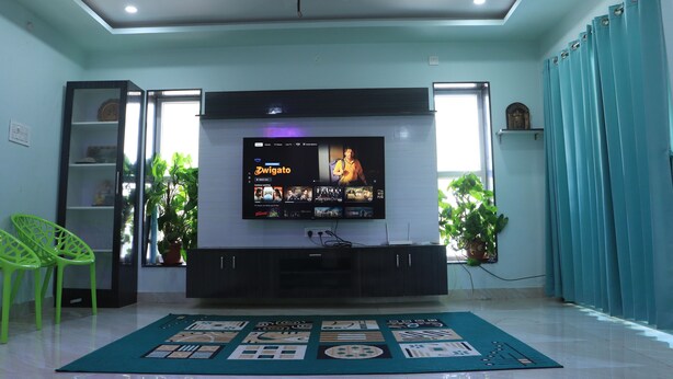 Een woonkamer met een flatscreen televisie aan de muur, een plafondventilator en een potplant.