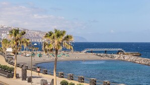 Eine Küstenpromenade mit Palmen, einem Strand und einem Felssteg.
