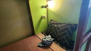 A small, narrow room with a single bed, a green wall, and a wooden ceiling. - Eyy Hostel (El Nido)