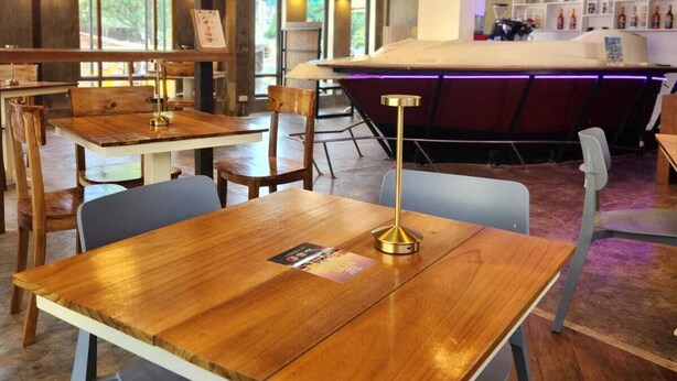 A restaurant with wooden tables and chairs, a bar area, and large windows allowing natural light. - Eyy Hostel (El Nido)