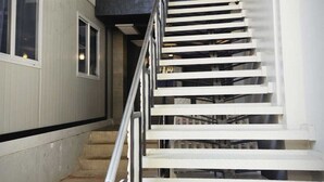 A staircase with metal railings and a concrete floor, leading to an upper level with a dark ceiling and exposed beams. - Eyy Hostel (El Nido)