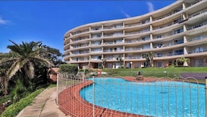 Un hotel de varios pisos con piscina, rodeado por una cerca de metal.