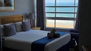 Habitación de hotel con cama, vista al océano, ventilador de techo y ventana con cortinas.