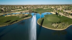 A golf course with a central water feature, surrounded by well-maintained grass and palm trees. - Entertainment Friendly Home in “The Grand” - Surprise, AZ! (Surprise)