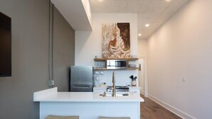 A modern kitchen with a central island, bar stools, a microwave, and a large decorative painting above the counter. - The Harriss (Wilson)