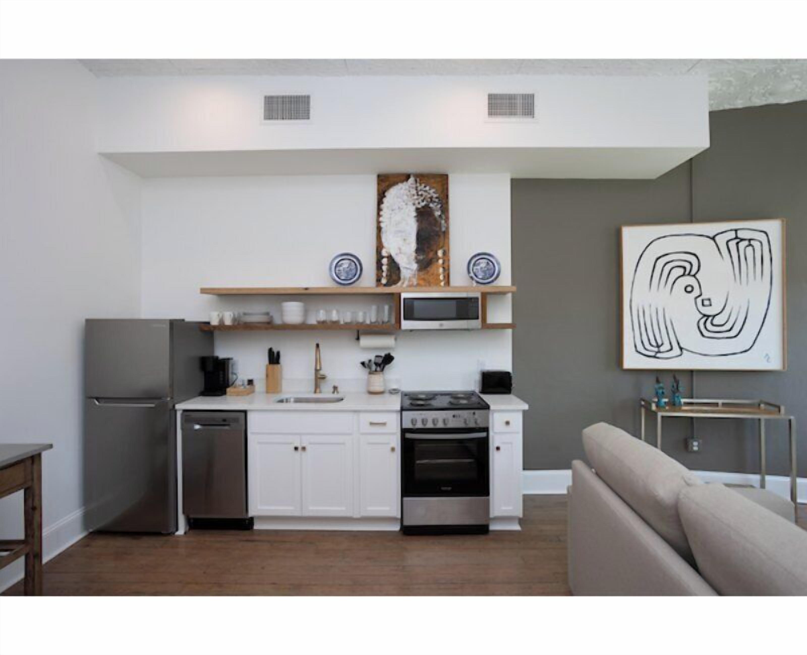A modern kitchen with white cabinets, stainless steel appliances, and a dining area with a grey sofa.