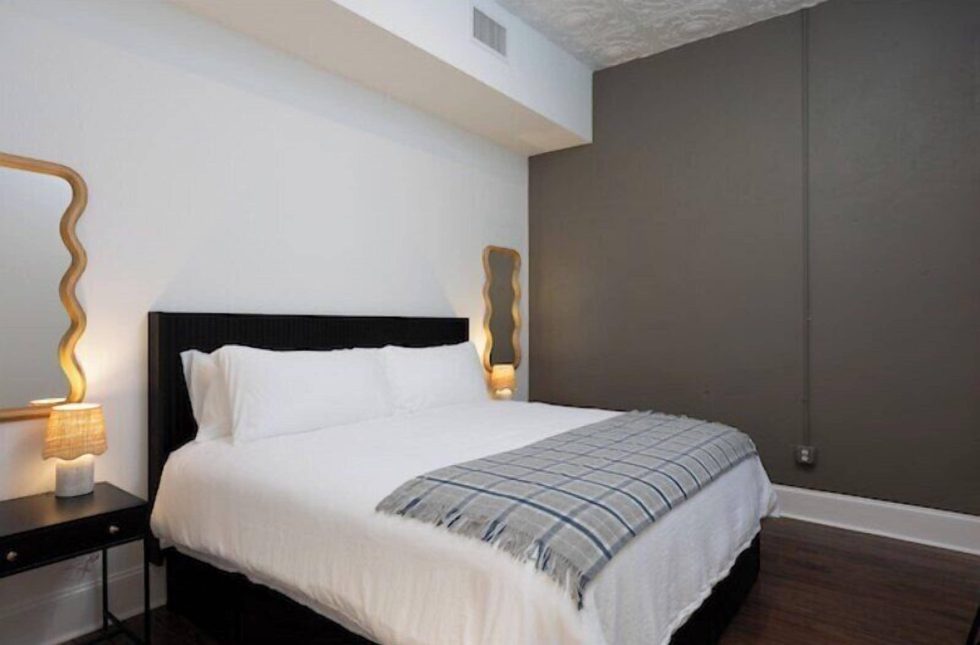 A bedroom with a large bed, a nightstand with a lamp, and a wall-mounted light fixture.
