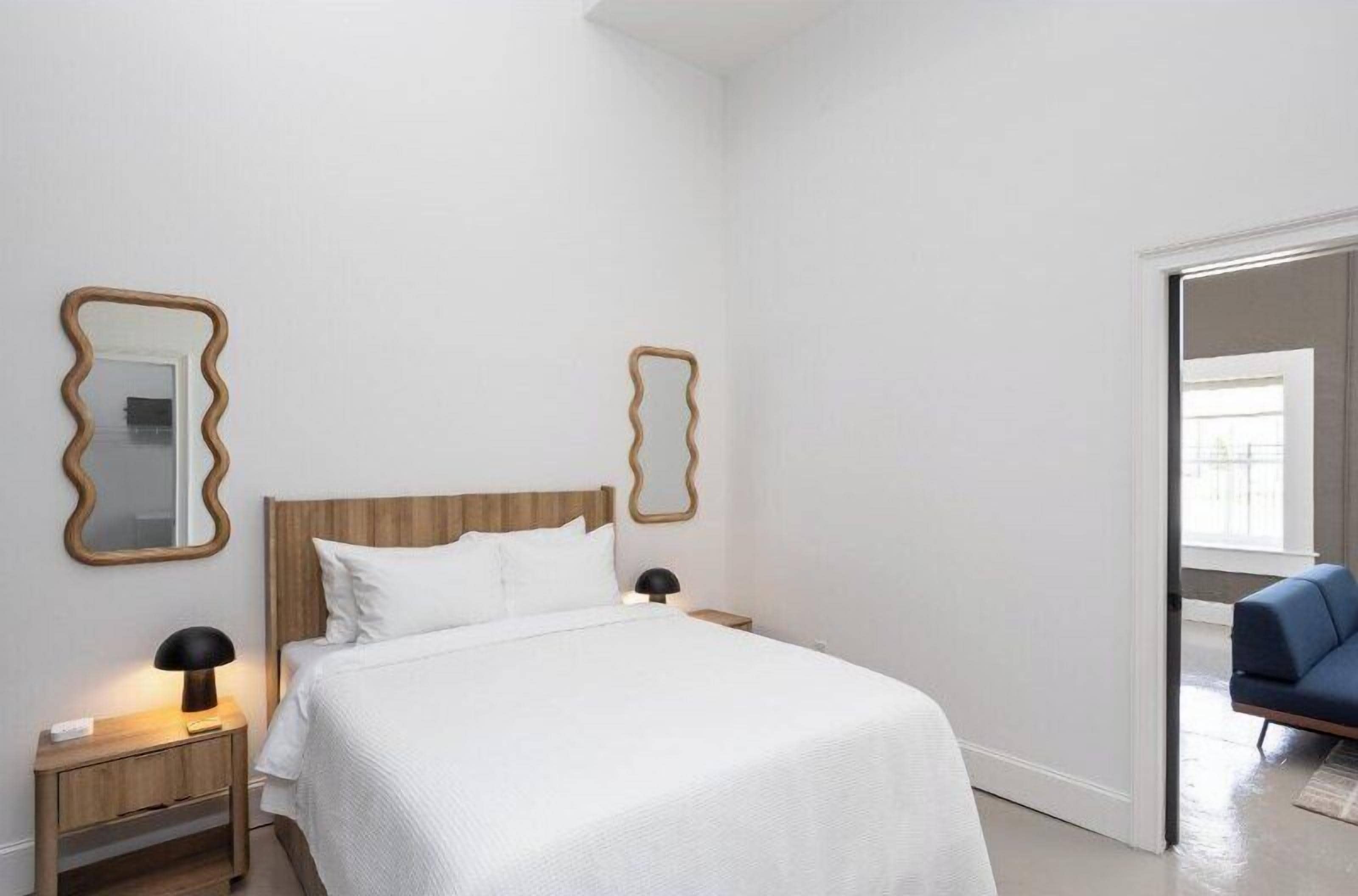 A bedroom with a wooden headboard, white bedding, two bedside lamps, and two wall-mounted mirrors.