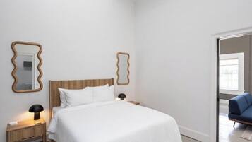 A bedroom with a wooden headboard, white bedding, two bedside lamps, and two wall-mounted mirrors.