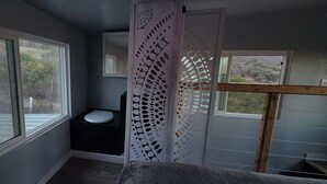 Une petite salle de bain comprenant des toilettes, une fenêtre et une porte ornée d’un motif décoratif.